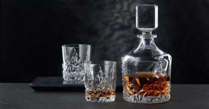 The NACHTMANN Sculpture Whiskey decanter besides the NACHTMANN Sculpture Whiskey tumbler, both of them filled with Whiskey. In the background an empty Sculpture tumbler on a serving tray.