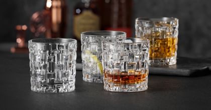 Four NACHTMANN Bossa Nova SOF glasses, three of them filled with either Whiskey or other drinks, one of them empty. In the background are liquor bottles.