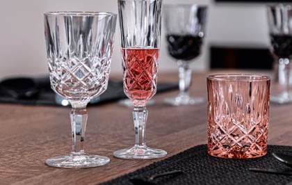 Le verre à cocktail à pied Noblesse de NACHTMANN, à côté de la coupe à champagne remplie de champagne rosé et du gobelet de couleur rosé.<br/>