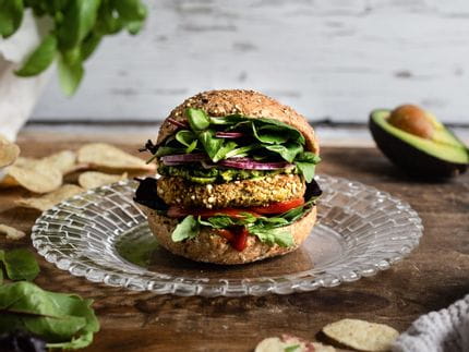 The small NACHTMANN Bossa Nova plate with a tasty Hamburger on a table, surrounded by salad leaves, potato chips, basil in a flower pot and an avocado.<br/>