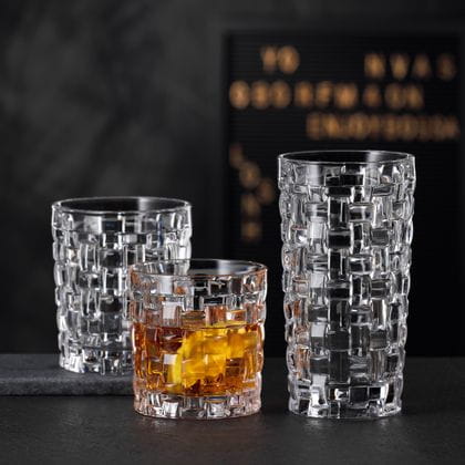 The NACHTMANN Bossa Nova SOF filled with whisky next to the empty Bossa Nova longdrink glass on a black stone sideboard. Behind them the empty Bossa Nova tumbler.<br/>