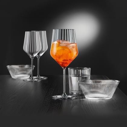 Filled NACHTMANN Aperitivo Spritz glass next to a drinking glass and bowl. Additional glasses and a bowl in the background.