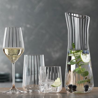 The SPIEGELAU Lifestyle series on a table. The filled red wine glass, the filled white wine glass, the filled Champagne glass, an empty longdrink glass, a tumbler filled with water, ice cubes and a slice of lime. On the right the carafe with infused water.<br/>