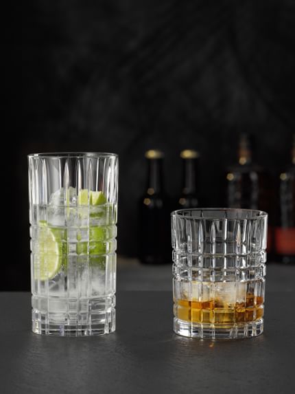 The NACHTMANN Highland Square longdrink glass filled with a clear drink with lime and ice cubes and the tumbler filled with Whiskey on the rocks.<br/>